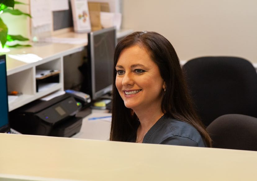 Meet the  {PRACTICE_NAME} Staff-Jennifer Lybrand smiling at the front desk